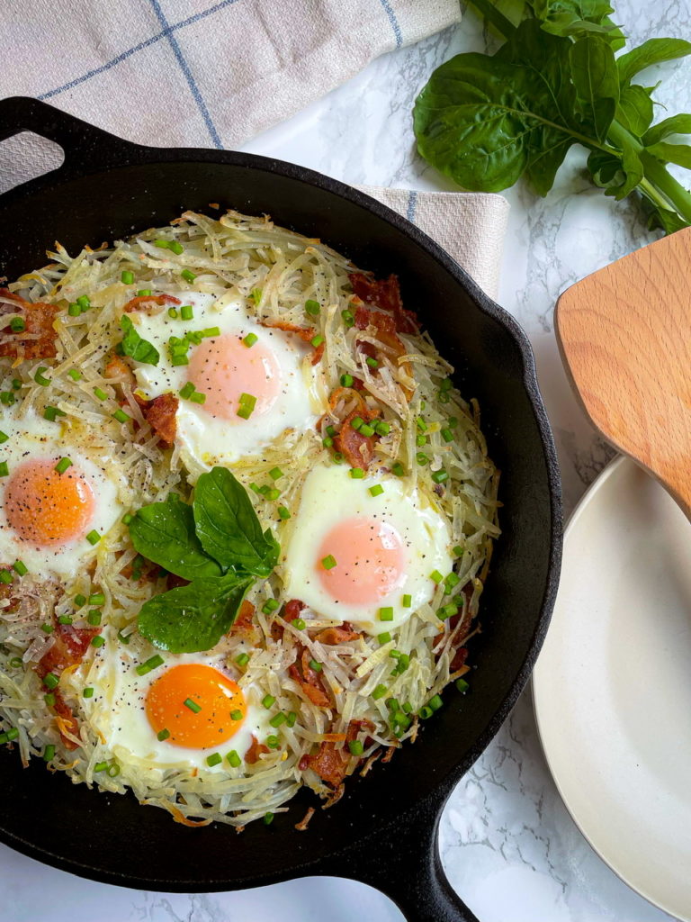 Frying pan with fried eggs and bacon on stove with fresh fruit and vegs  near by