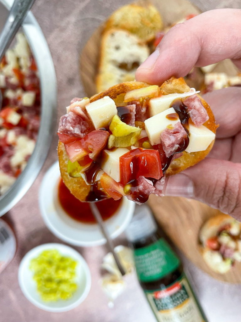 Antipasto Bites are crostini topped with salami, cheese, tomatoes, hot pepper, and balsamic glaze.