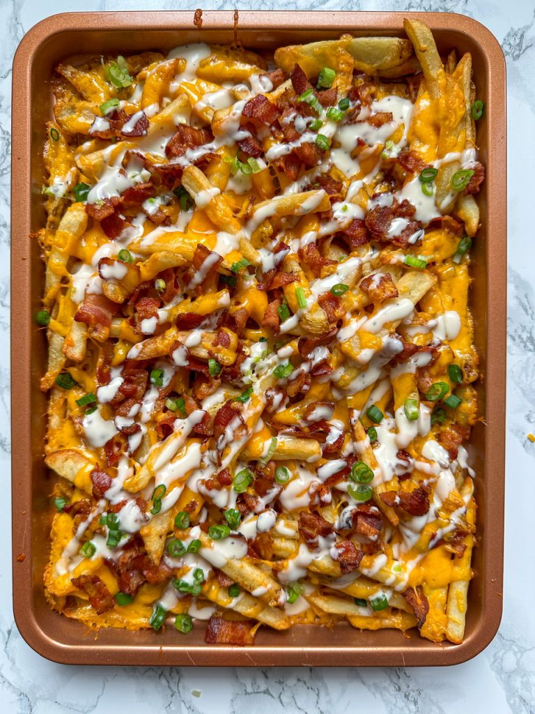 Loaded Fries baked on a sheet pan with cheese, bacon, and ranch dressing