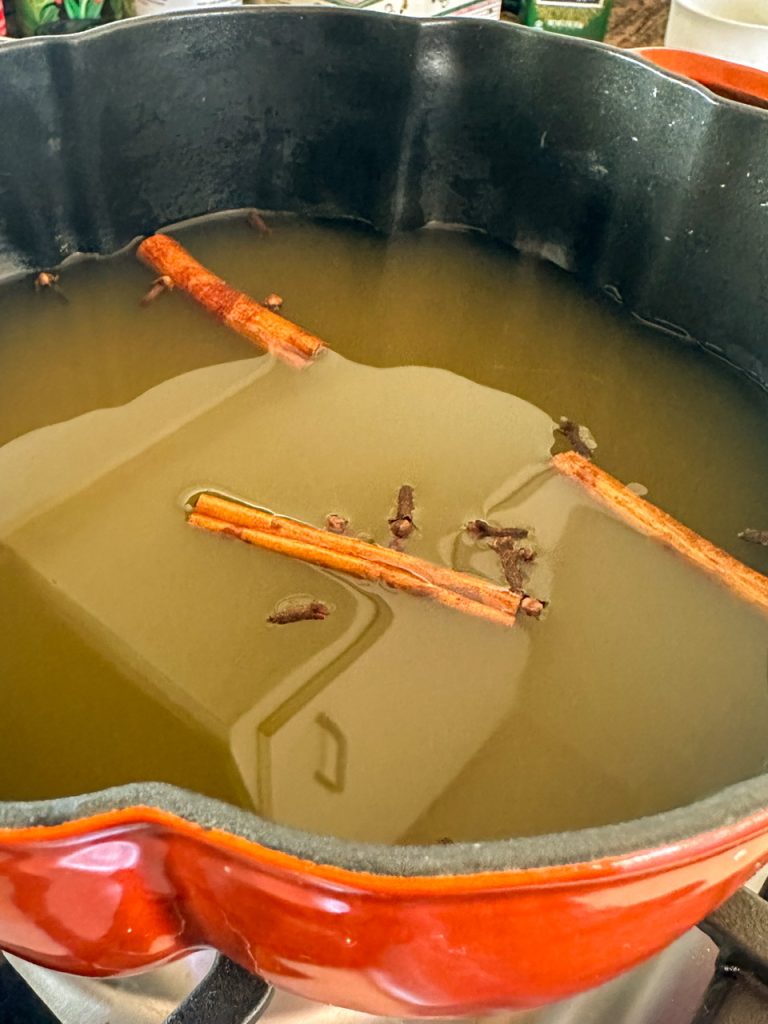 Apple Cider, cinnamon sticks, and whole cloves in a pot before it is set to boil.