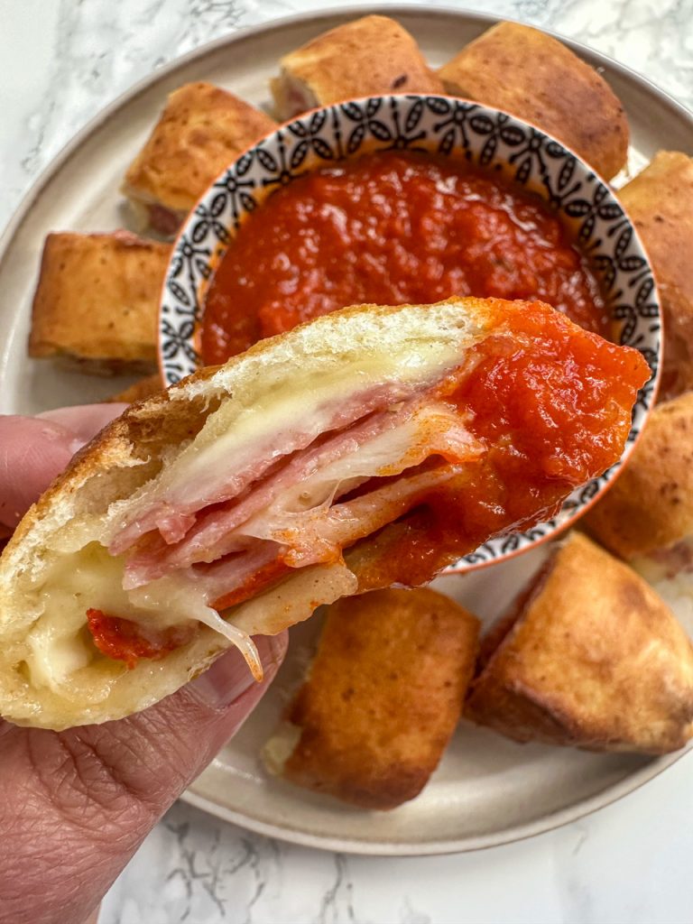 A deli stromboli filled with ham, salami, and cheese dipped into marinara sauce